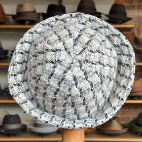 Tweed Sailor Cap in a black and white checked pattern displayed on a wooden stand with various other hats on shelves in the background.