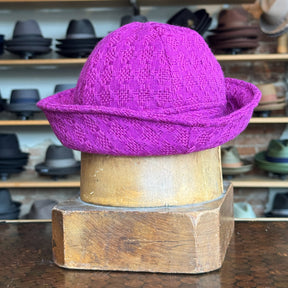 Tweed Sailor Cap in vibrant fuchsia with textured woven pattern, displayed on a wooden hat block, surrounded by various hats in the background.