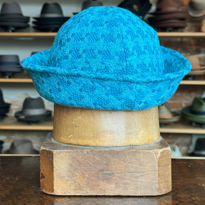 Tweed Sailor Cap in vibrant turquoise textured fabric displayed on a wooden hat stand with various hats in the background, showcasing a stylish accessory option.
