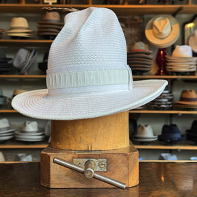 White on Rice Slouch Hat displayed on a wooden hat block with a wide brim and textured weave, surrounded by various hats on shelves in the background.