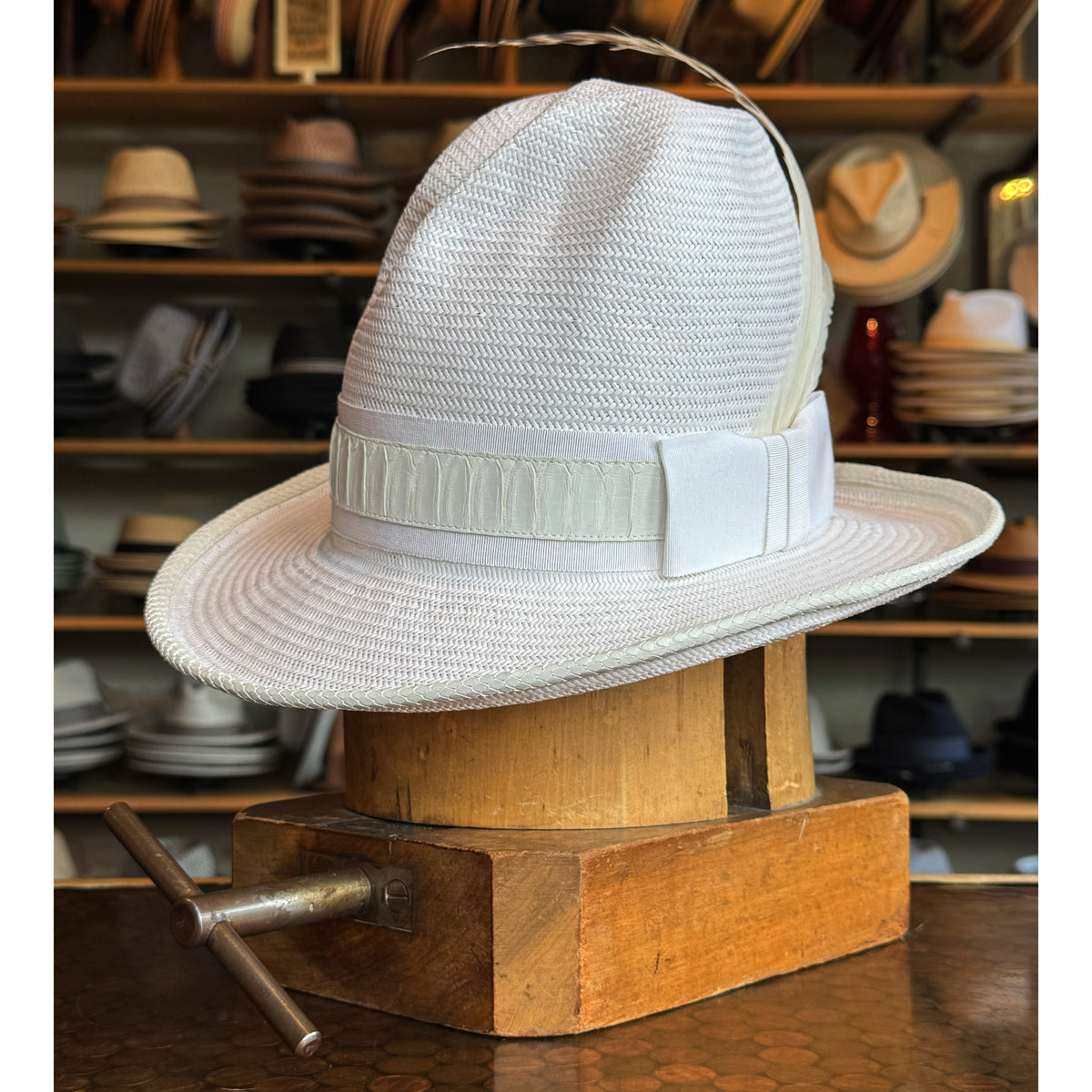 White on Rice Slouch Hat displayed on a wooden stand in a hat shop, featuring a textured weave and a wide ribbon band with a bow detail.