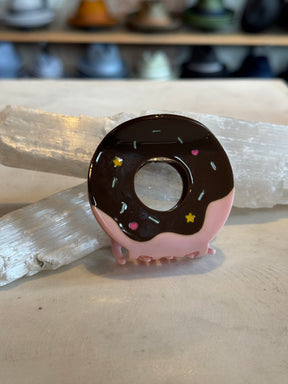 Donut Hair Clip designed with pink and chocolate glaze details, decorated with colorful sprinkles, resting on a neutral surface with a blurred background.