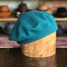 Side of Flora Beret displayed on a wooden hat stand, made of soft teal fabric, showcasing a classic French style accessory perfect for adding a chic touch to any outfit.