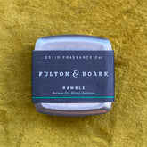 Square metal tin container of Solid Cologne with a black label displaying the fragrance name and natural scent notes on a textured yellow surface