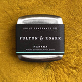 Solid Cologne in a sleek metal case on a textured mustard yellow background, featuring a black label with white text highlighting the Mahana scent notes.