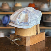 Pattern Patch Hatteras newsboy cap in soft neutral patchwork fabric, displayed on a wooden hat block with a blurred hat shelf background, showcasing vintage-inspired style.