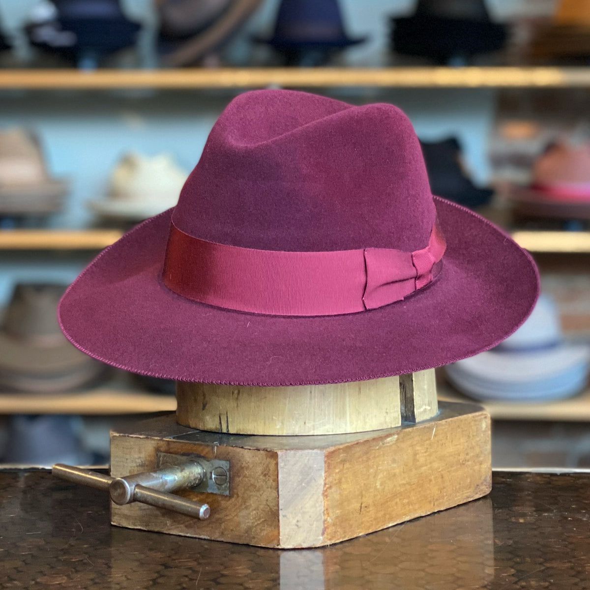Special Edition Daniel hat in rich burgundy with a wide brim and matching ribbon band, displayed on a wooden hat block in a vintage shop setting.